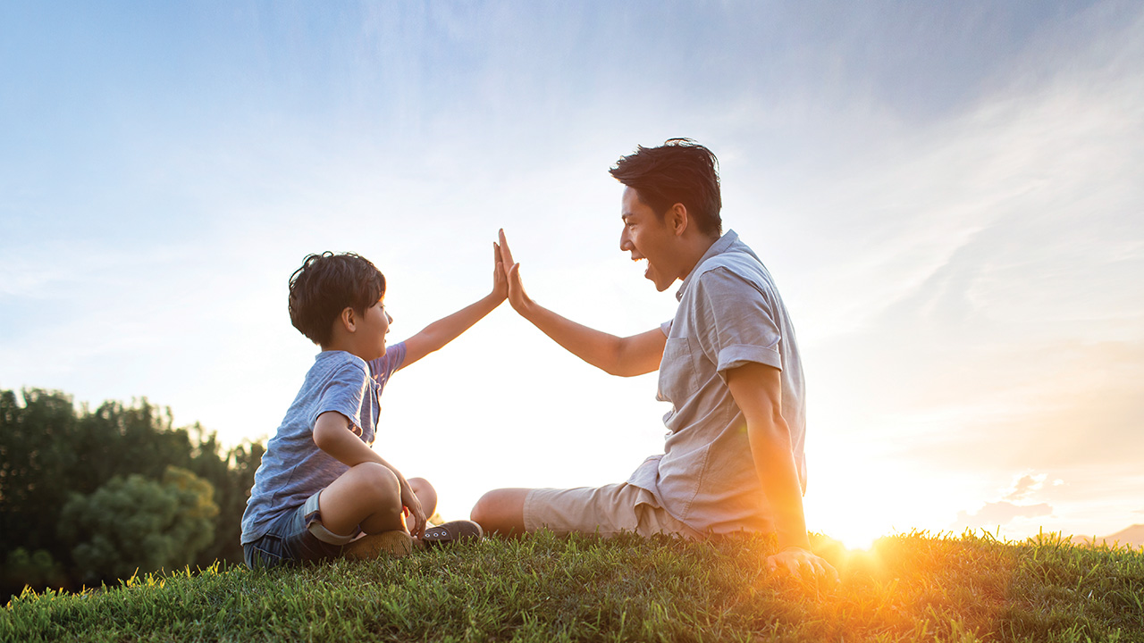 A father and son giving each other a high five on meadow; image used for HSBC Singapore Insurance Legacy.