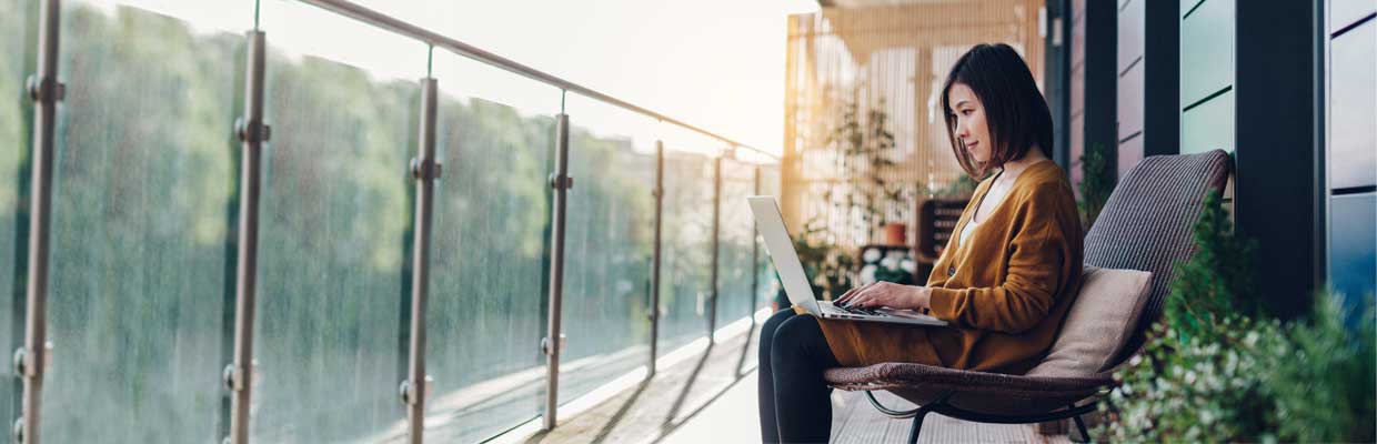 A woman working on laptop on balcony; image used for HSBC Singapore New Payment page.