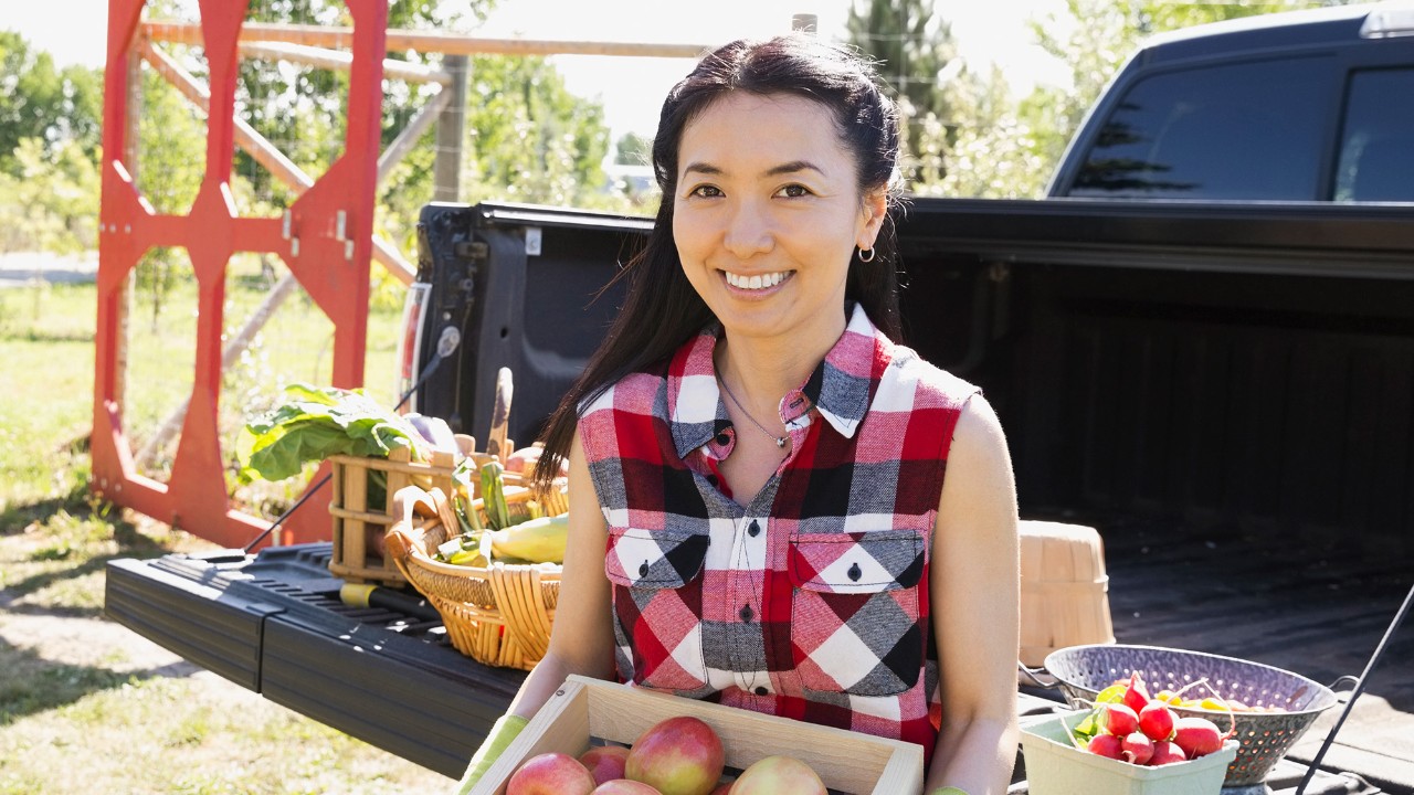 Woman holds a wooden carton of apples with natural produce in a truck in the background; image used for HSBC Investments Funds.
