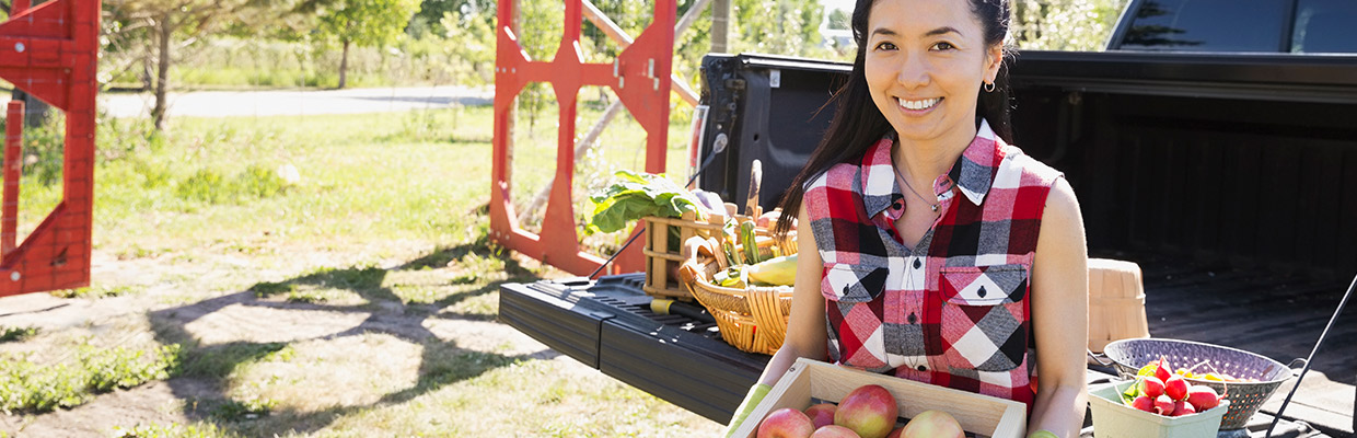 Woman holds a wooden carton of apples with natural produce in a truck in the background; image used for HSBC Investments Funds