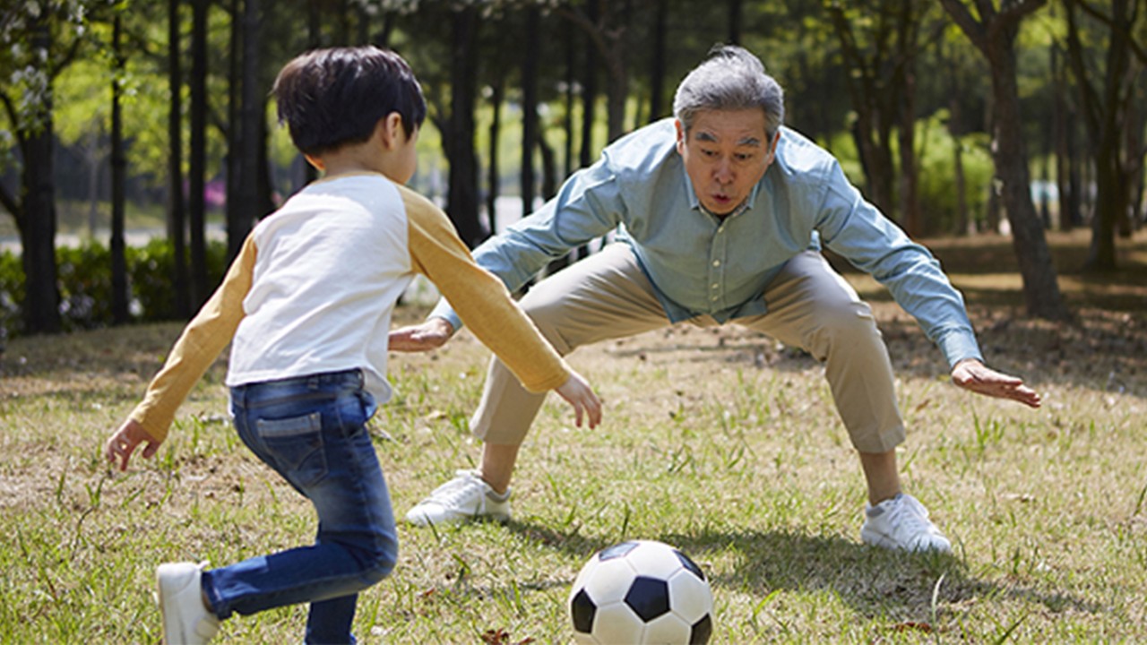 A grandfather and grandson are playing football; image used for HSBC Singapore Goal Protector page.